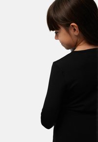 Camisa negra de manga larga con cuello redondo, textura suave, diseño ajustado y acabado liso; llevada por un niño de espaldas a la cámara.