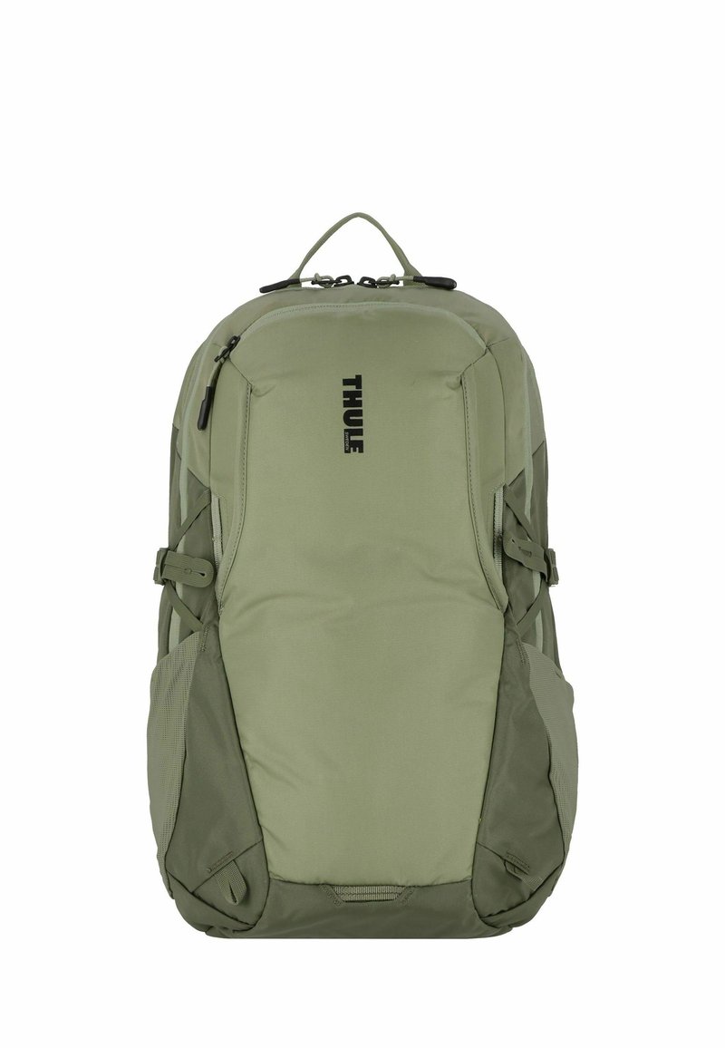 Sac à dos Thule vert olive avec un design épuré. Il dispose de poches latérales rembourrées, de bretelles réglables et d'une poignée de transport supérieure. Logo imprimé à l'avant.