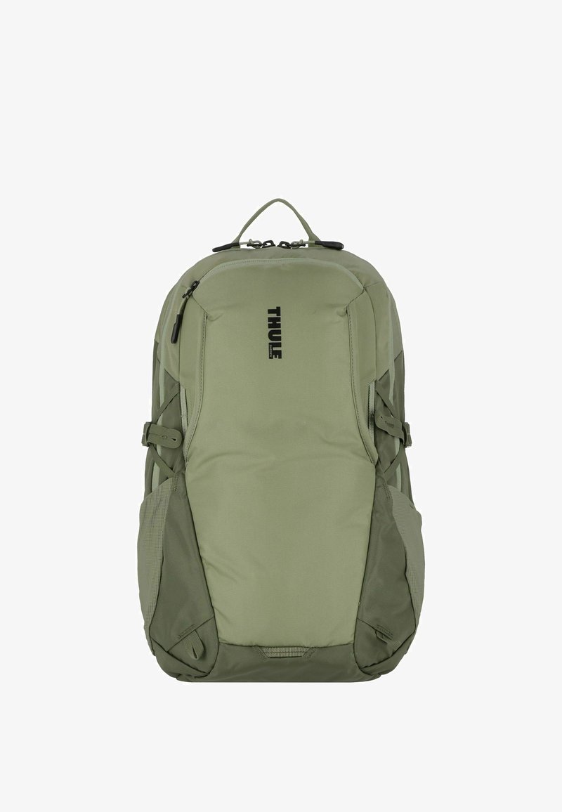 Sac à dos Thule vert olive avec un design épuré. Il dispose de poches latérales rembourrées, de bretelles réglables et d'une poignée de transport supérieure. Logo imprimé à l'avant.