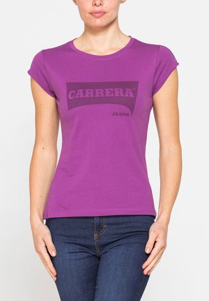 Donna che indossa una maglietta viola a maniche corte con il logo "CARRERA Jeans" e jeans blu scuro, in piedi con le mani rilassate lungo i fianchi.