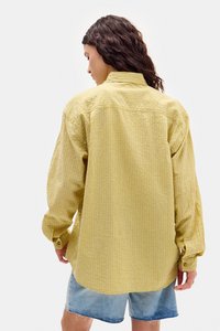 Żółta koszula w kratę z długim rękawem, z guziczkami na mankietach i luźnym krojem, w połączeniu z wyblakłymi szortami dżinsowymi.