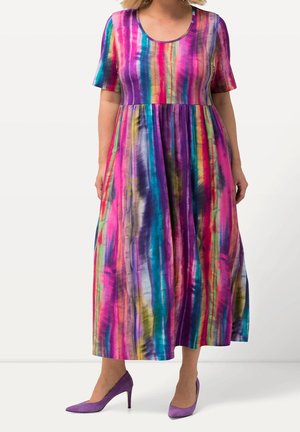 Femme portant une robe maxi aux rayures verticales colorées avec des manches courtes, associée à des escarpins violets à bout pointu.