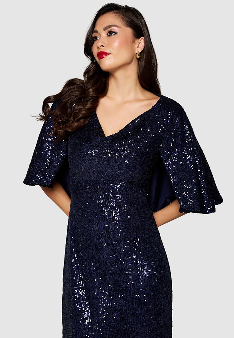 Robe en sequins navy avec un décolleté en V et des manches évasées. Le tissu est scintillant, ajoutant de la texture et de l'intérêt visuel.
