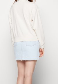 Krämfärgad, överdimensionerad sweatshirt med ribbade mudd, tillsammans med en ljusblå denim minikjol med fransar och två bakfickor.