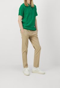 Zielona, dzianinowa koszulka polo z krótkim rękawem, połączona z beżowymi chinosami i białymi sneakersami, o luźnym kroju i teksturowanym wzorze.