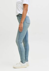 Wąskie dżinsy wykonane z jasnoniebieskiego denimu, o dopasowanym kroju, standardowych kieszeniach i wysokim stanie, zestawione z białymi sneakersami.