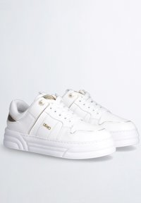 Sneakers bianchi in pelle con una suola bianca spessa, dettagli dorati sul tallone e design con lacci. Superficie strutturata con dettagli di cucitura.