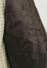 Chaqueta acolchada marrón con una textura suave, que presenta un bolsillo lateral, cierre de cremallera y un forro de cuadros en contraste.