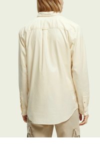 Crème kleurige lange mouwen shirt van zacht katoen, met een gebogen zoom, knoopmanchetten en een rugplooien voor extra beweging.