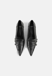 Ballerines en cuir noir à bouts pointus avec trois brides à boucles argentées sur chaque chaussure, présentées côte à côte sur un fond blanc.