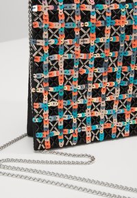 Schwarze Handtasche mit einem geflochtenen Design aus bunten Schlaufen in Pfirsich, Blau und Creme, verziert mit metallischen Akzenten und einem silbernen Kettenriemen.
