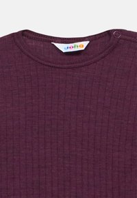 Maglietta per neonati viola a coste con scollo rotondo e chiusura con bottoni a pressione sulle spalle, con una piccola etichetta colorata del marchio all'interno del colletto.