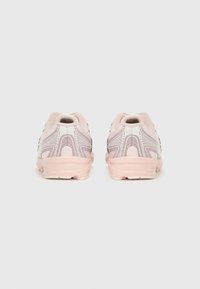 Fehér és rózsaszín sportcipő pár hátulnézetből, mintás részletekkel és párnázott talppal, fehér háttéren.