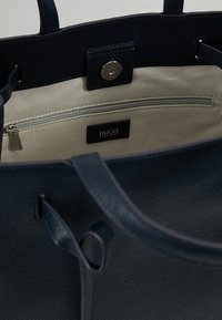 Borsa tote in pelle testurizzata blu navy con due manici, foderata in tessuto beige, con tasca interna con zip e targhetta con logo.