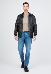 Svart läderjacka med dragkedja, två bröstfickor, beige rundhalsad tröja, blå jeans och svarta snörstövlar. Enkel och strukturerad design.