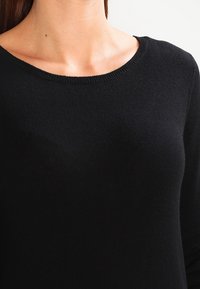 Pull noir en maille avec un col rond, texture légère et manches longues. La vue en gros plan met en avant le tissu lisse et la forme.