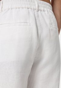 Witte linnen broek met een elastische tailleband, voorzien van twee achterzakken en een gestructureerd oppervlak, dat een lichte en ademende uitstraling heeft.