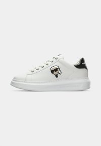 Vit låg sneaker med tjock sula, svart hälflik och en tecknad ansikte med solglasögon på sidopanelen, snörning.