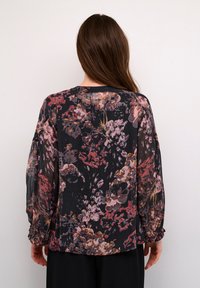 Luftige Bluse aus transparentem Stoff mit schwarzem Grund, ausgestattet mit einem bunten Blumenmuster in verschiedenen Pink-, Lila- und Rottönen. Elastische Bündchen.