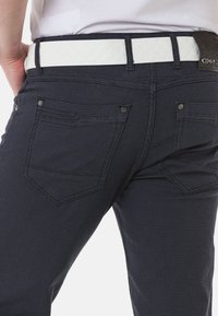 Marineblau karierte Hose mit tailliertem Schnitt, ausgestattet mit einem weißen strukturierten Gürtel und zwei Gesäßtaschen mit silbernen Hardware-Akzenten.