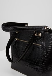 Sac à main noir embossé crocodile avec une texture brillante, une quincaillerie dorée, des anses doubles et un détail de poche avant zippée.