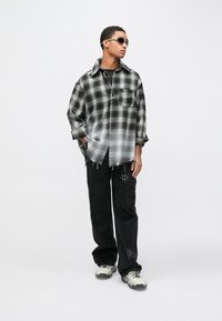 Svart och grå rutig oversize-skjorta med sliten fåll och framficka. Matchas med lösa svarta byxor med nitar. Vita sneakers.