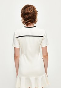 Ärmelloses Kleid aus cremefarbener Stoff mit tailliertem Oberteil und ausgestellt Saum, mit schwarzem Besatz am Ausschnitt und Rücken.