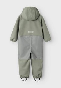 Groene waterdichte overall met een grijze onderkant, voorzien van een capuchon, elastische manchetten en een reflecterende stip op de achterkant. Verstelbare voetbanden.