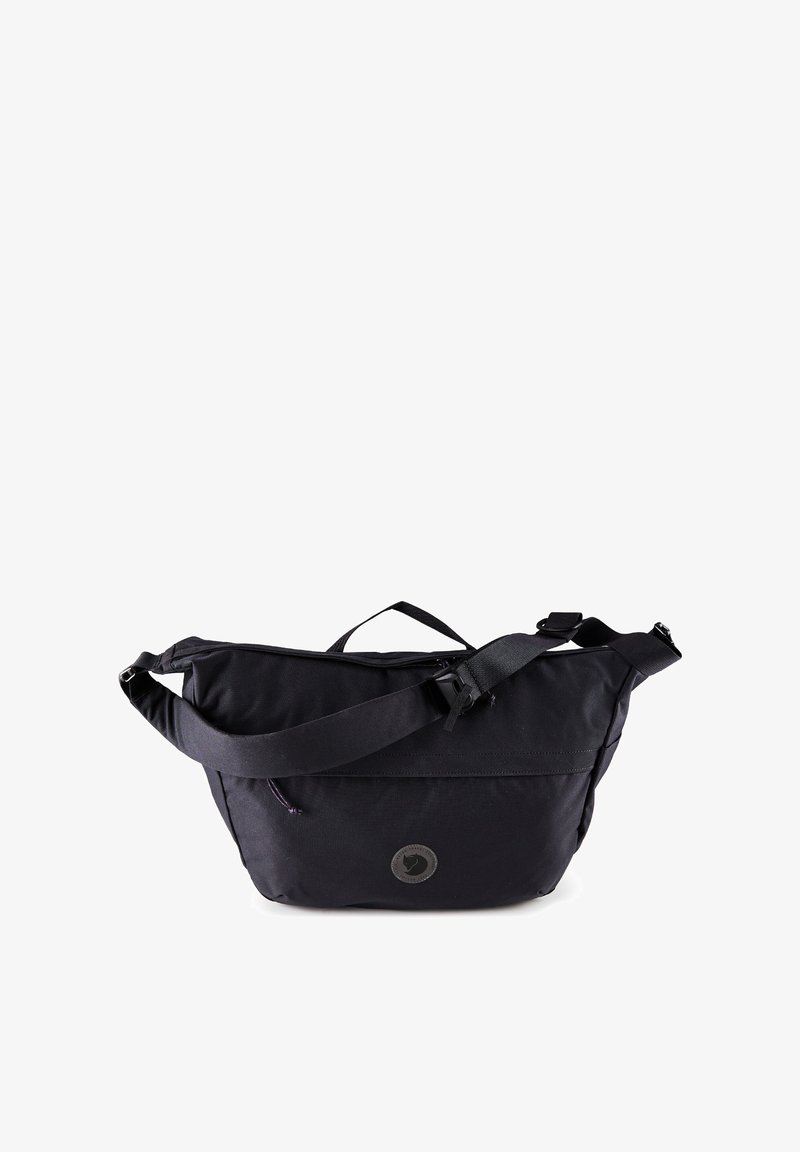 Sort crossbody-task med justerbar skulderrem, øverste håndtag, lynlåslomme foran og rundt logo-patch midt på fronten.