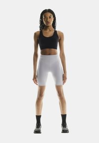 Zwarte sportbeha, lichtgrijze high-waisted shorts, aansluitend ontwerp, gladde textuur, minimale branding op de shorts, sportschoenen met donkere accenten.