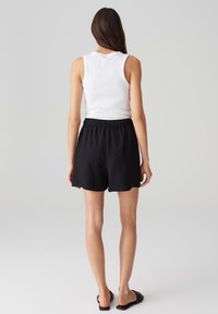 Bílý bezramínkový top v kombinaci s černými skládacími šortkami se elastickým pasem. Šortky mají volný střih a hladký povrch.