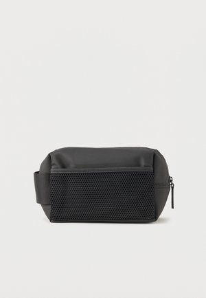 Trousse de toilette rectangulaire noire avec poche avant en filet, poignée latérale et fermeture éclair sur fond blanc.