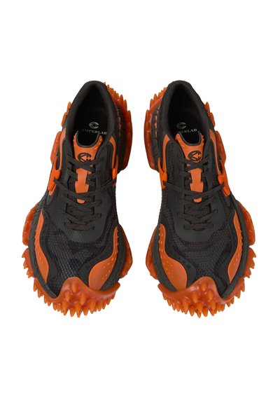 Schwarze und orangefarbene Sneaker mit strukturiertem Mesh-Obermaterial und klobigen, gezackten orangen Sohlen, von oben betrachtet, die das Schnürdesign zeigen.