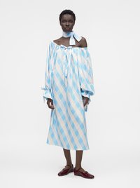 Γυναίκα που φοράει μπλε-λευκό καρό φόρεμα με έξω τους ώμους και φουσκωτά μανίκια, ταιριαστό μαντήλι στον λαιμό και σκούρα κόκκινα παπούτσια Mary Jane.