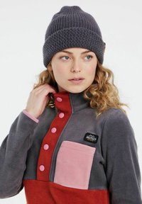 Fleece pullover in grijs, rood en roze, met een hoge kraag, decoratieve knopen en een borstzak met een logo patch. Gezellige gebreide beige beanie.
