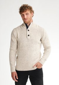 Maglione lavorato a maglia di colore beige chiaro con tessuto texturizzato, apertura con bottoni, polsini a coste e un leggero motivo maculato.