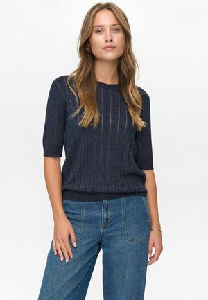 Pull en tricot bleu marine à manches courtes, avec des rayures verticales et un col rond. Porté avec un jean bleu taille haute.