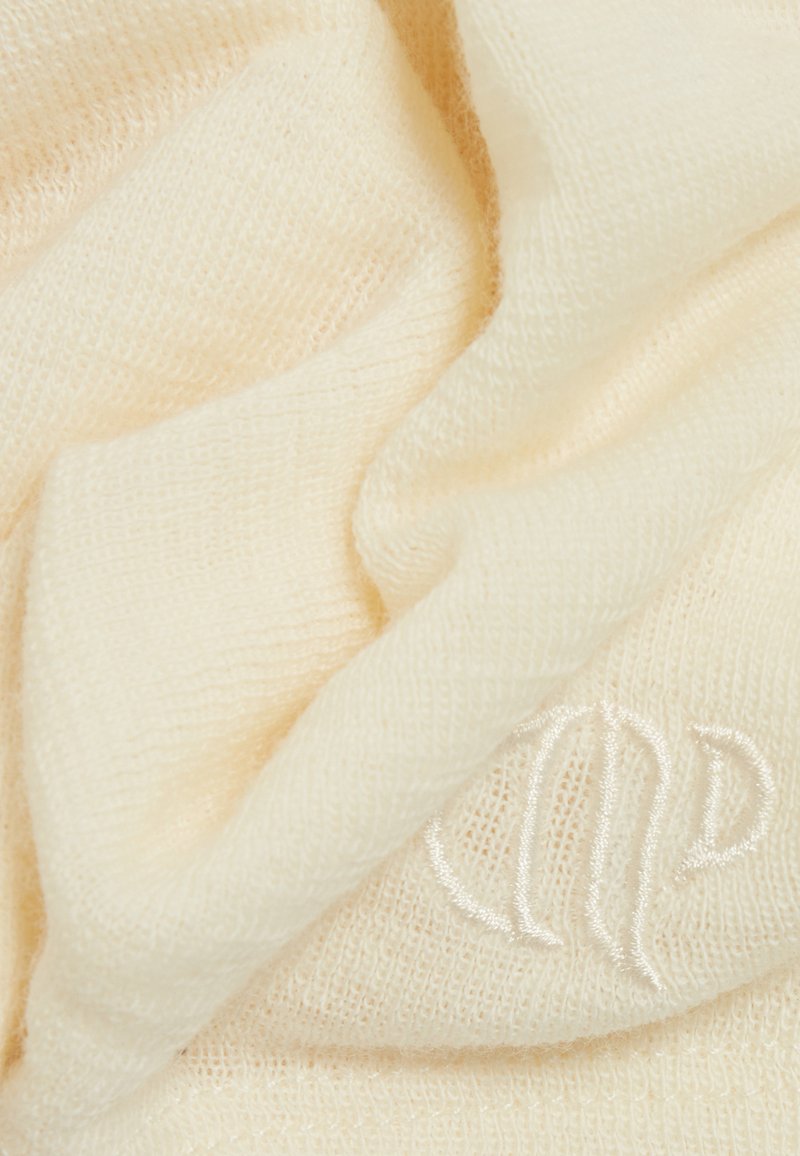 Licht crèmekleurige gebreide sjaal, zachte textuur, met een geborduurd logo in een iets donkerdere tint. De stof is luchtig en heeft een fijne weving.
