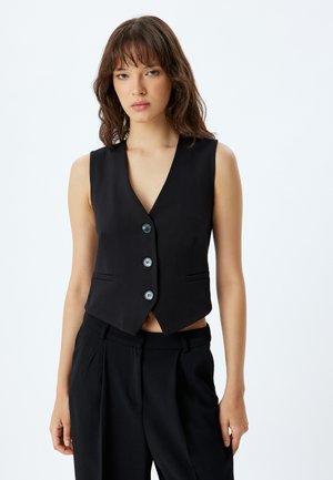 Gilet sans manches noir avec un décolleté en V profond, cinq boutons et deux poches latérales, fabriqué en tissu lisse avec une coupe ajustée.