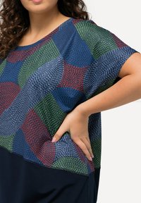 Top de manga corta con un patrón texturizado multicolor que presenta secciones en rojo, verde y azul, que transicionan a un fondo azul marino sólido.