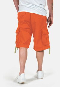 Pantaloni cargo arancioni in cotone con molteplici tasche laterali, cordini regolabili all'orlo e una patch con logo su una gamba.
