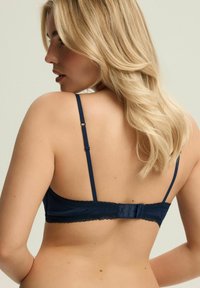 Granatowy koronkowy biustonosz z regulowanymi ramiączkami, falbankami na brzegach i zapięciem na haftkę. Gładka tekstura z delikatnym wykończeniem z tyłu.