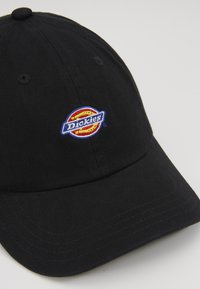 Fekete pamut baseball sapka, amelyen hímzett kör alakú logó található "Dickies" felirattal kék és piros színben, a karimán ívelt varrással kiemelve.
