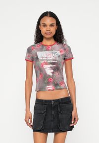 Tričko s krátkym rukávom zdobené flitrami s kvetinovým vzorom v odtieňoch ružovej, s okrúhlym výstrihom a červeným lemom. Nosené s čiernou džínovou sukňou.