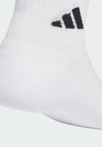 Calcetín deportivo blanco hecho de tela acanalada con punta reforzada; cuenta con detalle del logo de Adidas en negro cerca de la parte superior.