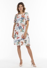 Witte bloemenprint jurk met blauwe, oranje en groene bladeren. Korte mouwen, een strik in de taille en een gerimpelde zoom voegen detail toe.