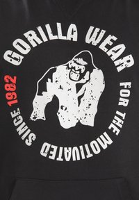 Zwarte hoodie met witte versleten tekst en een gorilla-afbeelding. Bevat "Gorilla Wear" en "Sinds 1982" in het rood, met een kangoeroezak.