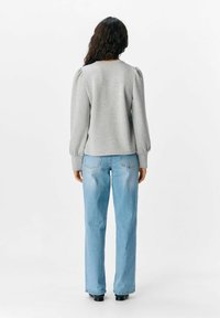 Grijze sweatshirt met pofmouwen, ronde hals en gestructureerde stof, gecombineerd met lichtblauwe rechte jeans en zwarte enkellaarzen.