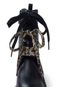 Botín de cuero negro con un acabado brillante, con cordones de leopardo en beige y cordones de textil negros, que presenta una puntera redonda y una lengüeta.