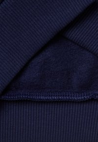 Il tessuto del maglione blu navy presenta una texture a costine all'esterno e un rivestimento morbido e peloso all'interno. Orli cuciti con precisione alla base.